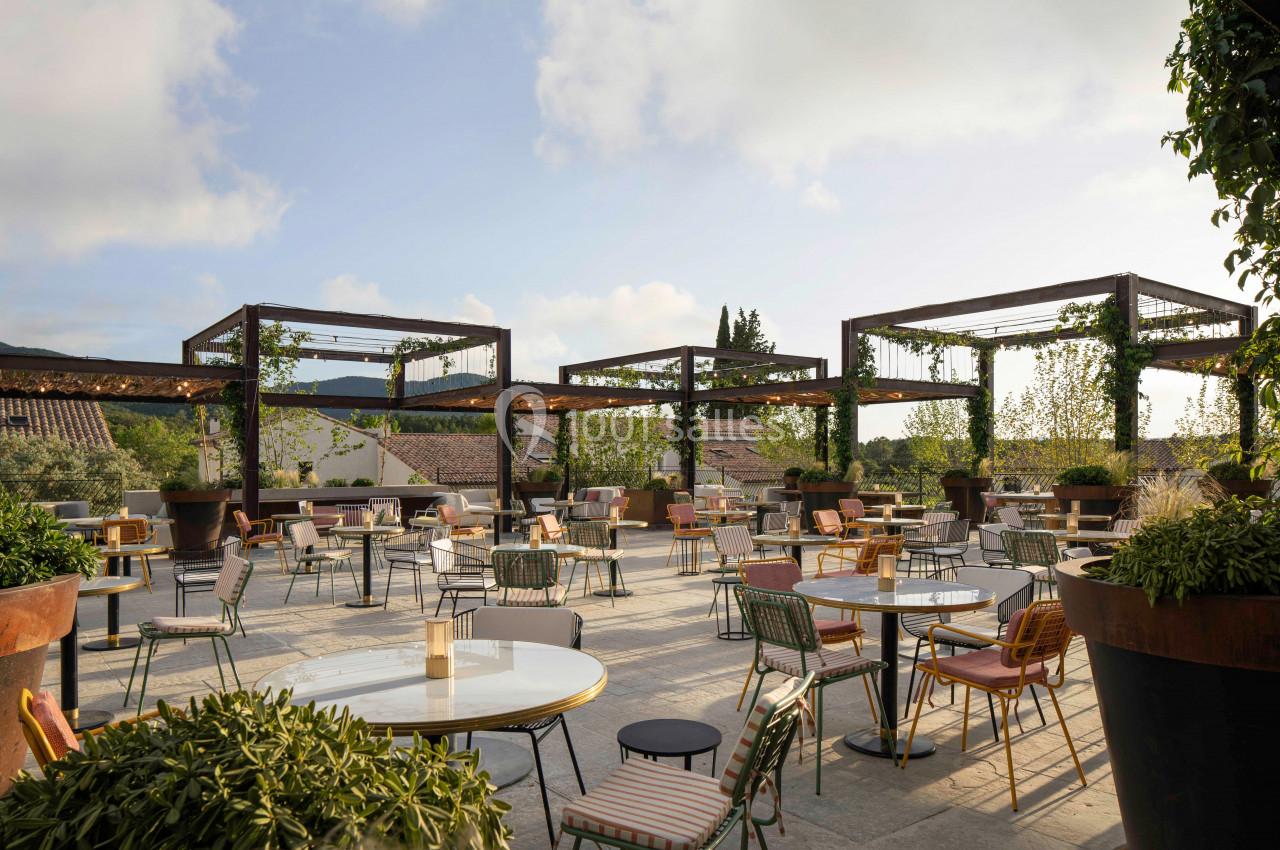 Terrasse extérieure aménagée avec des tables et des chaises, entourée de plantes et de structures en bois.