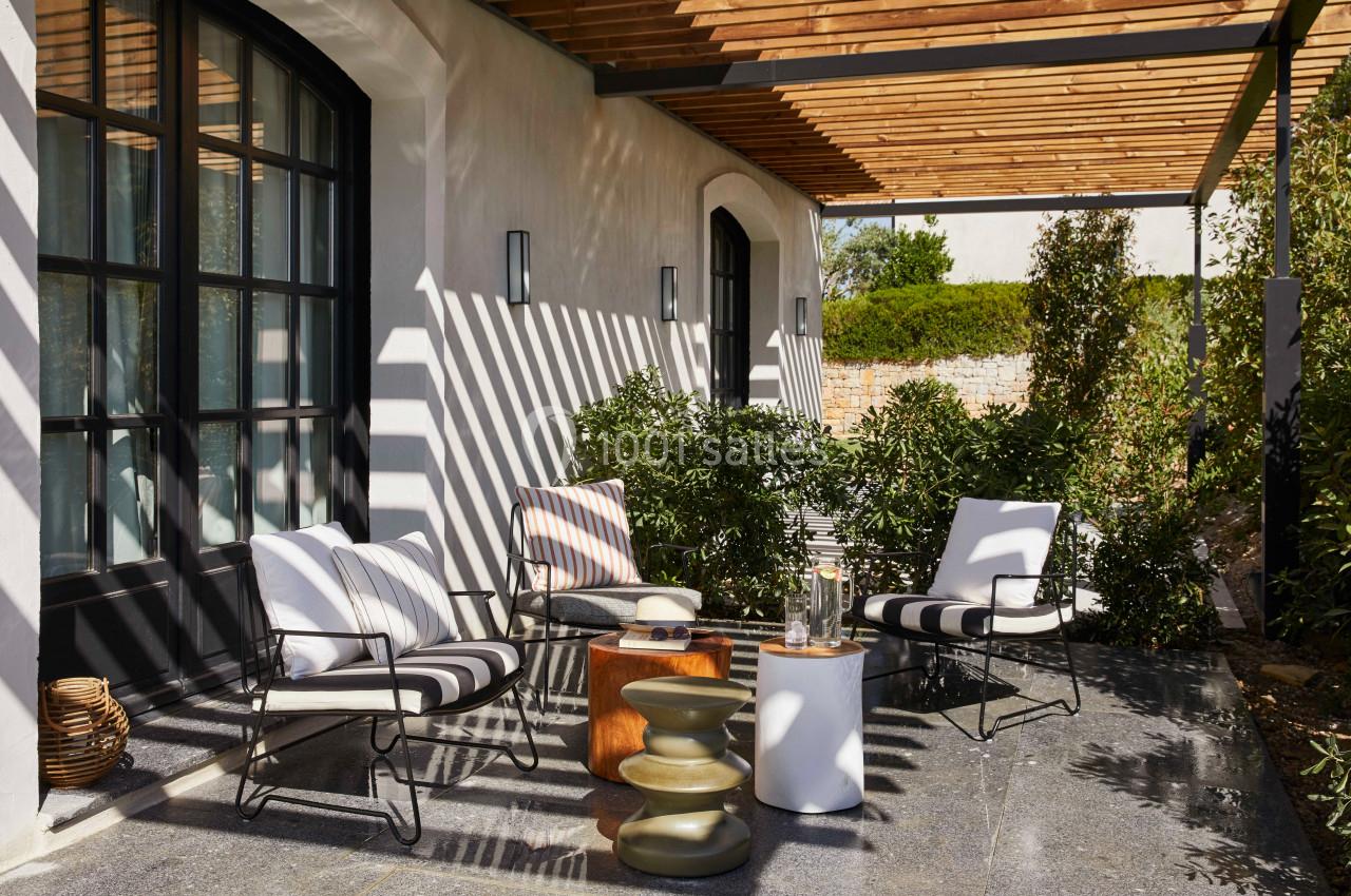 Terrasse ombragée avec mobilier de jardin moderne, coussins rayés, tables d'appoint et plantes environnantes.