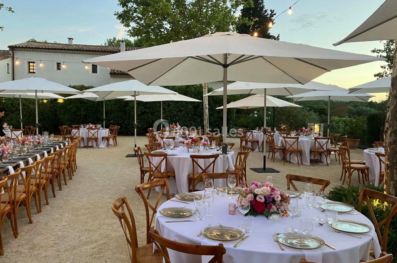 Tables élégamment dressées avec des nappes blanches et des bouquets de fleurs, disposées en extérieur sous des parasols.