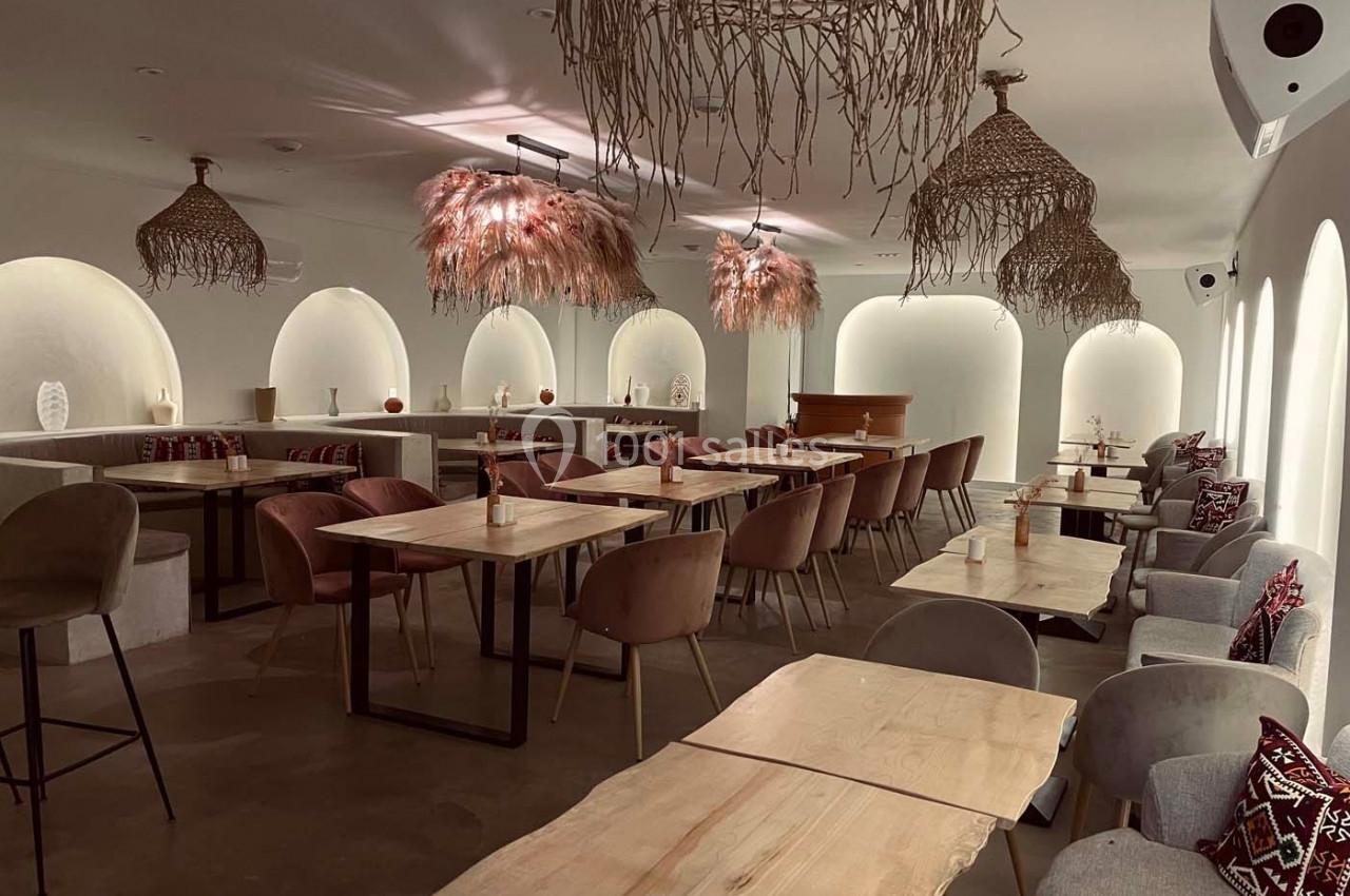 Salle de restaurant lumineuse avec tables en bois clair, chaises rembourrées et suspensions en fibres naturelles.