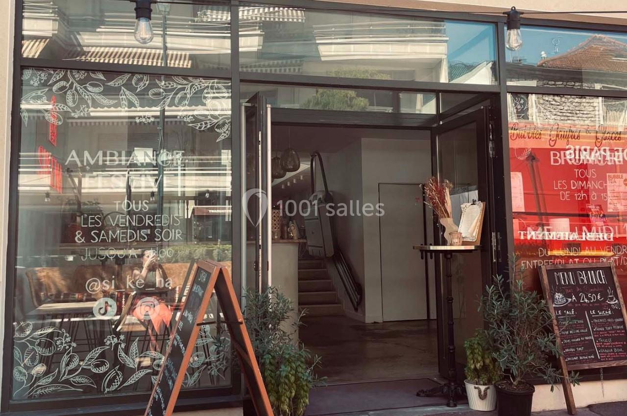 Façade d'un établissement avec vitrines décorées, porte ouverte et panneaux d'information sur le trottoir.