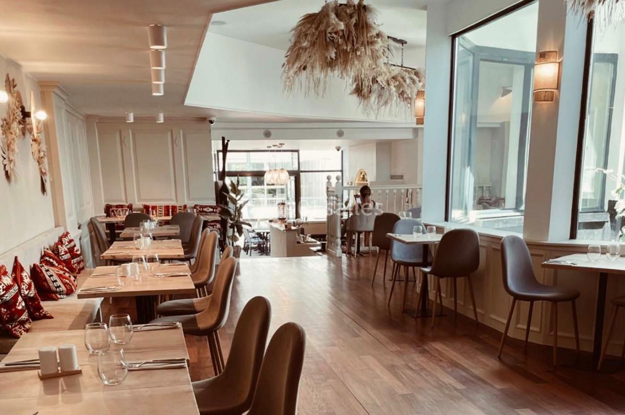 Salle de restaurant lumineuse avec tables en bois, chaises modernes et décoration suspendue en fibres naturelles.