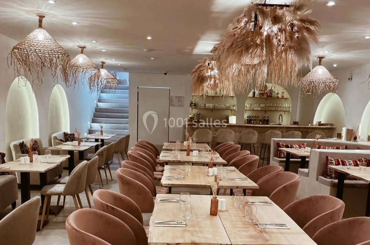 Salle de restaurant lumineuse avec tables en bois, chaises rembourrées et suspensions décoratives en fibres naturelles.