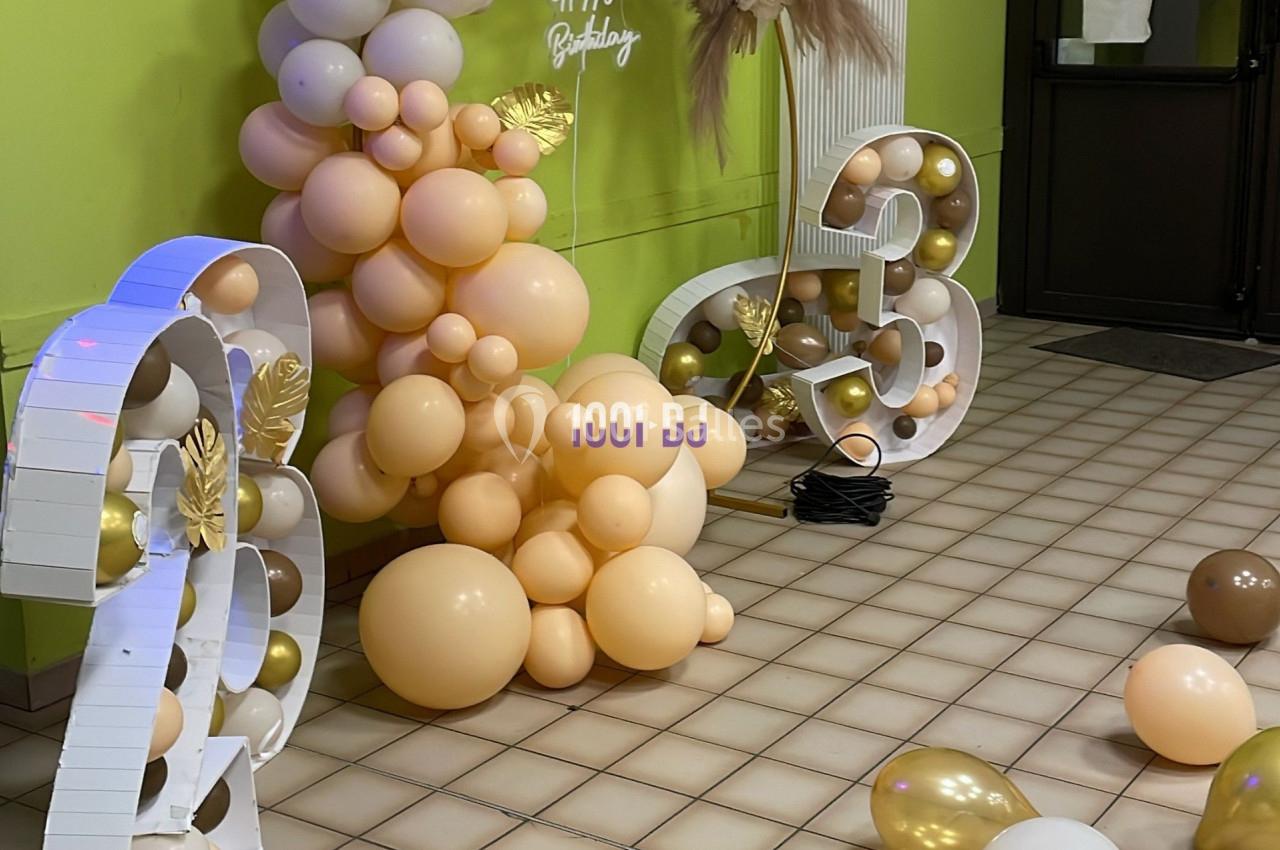 Décoration d'anniversaire avec arche de ballons beige et marron, chiffres lumineux et ballons dorés au sol.