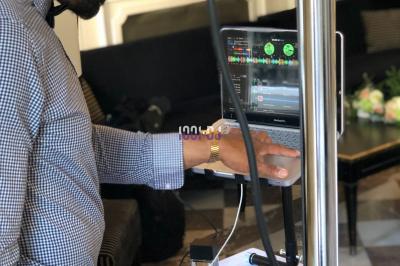 Un DJ souriant derrière une table équipée de matériel audio, avec un ordinateur portable et une table de mixage.