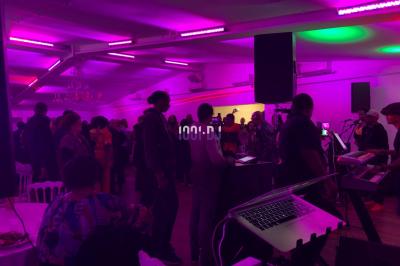 Un DJ souriant derrière une table équipée de matériel audio, avec un ordinateur portable et une table de mixage.