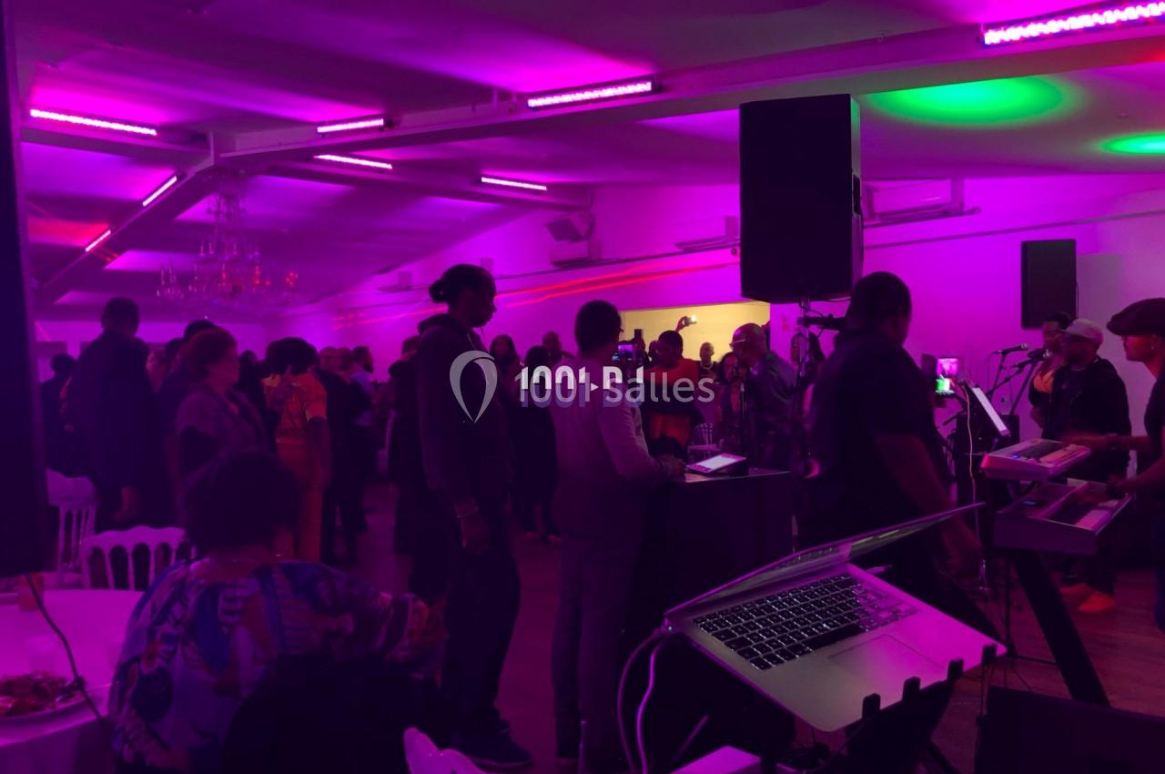 Groupe de personnes dans une salle éclairée par des lumières colorées, avec un DJ et du matériel audio visible au premier…