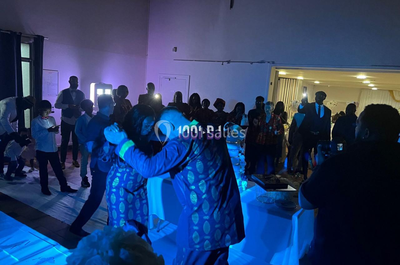 Un couple danse sous une lumière bleue devant des invités dans une salle de réception.