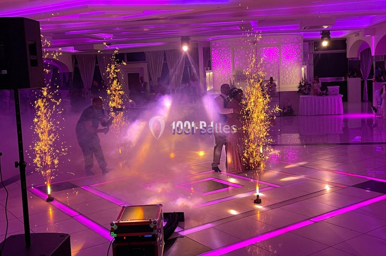 Un couple danse au centre d'une salle éclairée par des lumières violettes et des étincelles décoratives.
