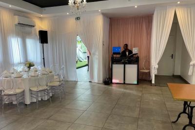 Un DJ souriant derrière une table équipée de matériel audio, avec un ordinateur portable et une table de mixage.