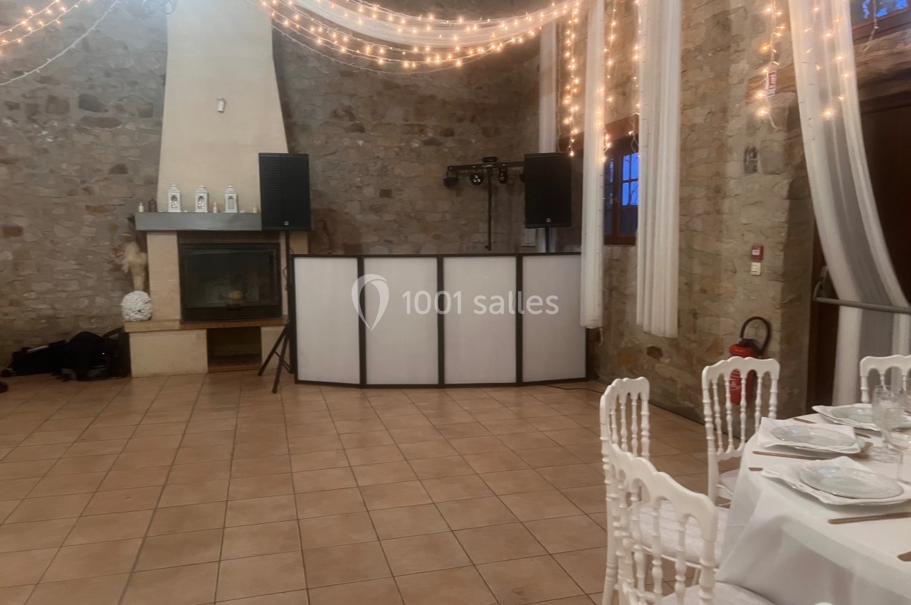 Salle en pierre décorée de guirlandes lumineuses avec une table dressée et un espace DJ équipé de haut-parleurs.