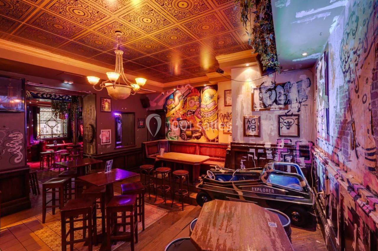 Intérieur d'un bar avec des murs décorés de graffitis, des tables en bois et un plafond orné de motifs dorés.