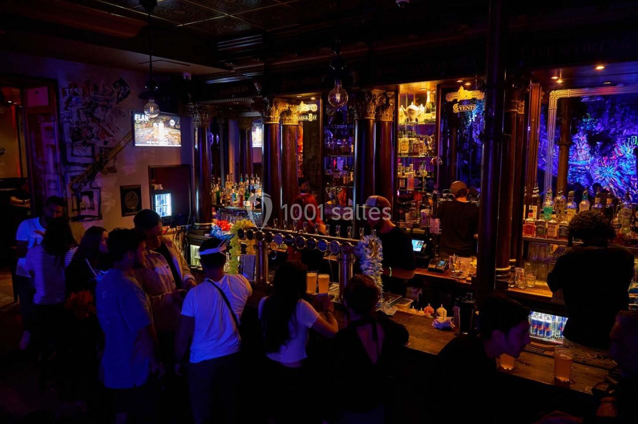 Des personnes discutent et commandent des boissons dans un bar à l'éclairage tamisé avec un comptoir en bois.