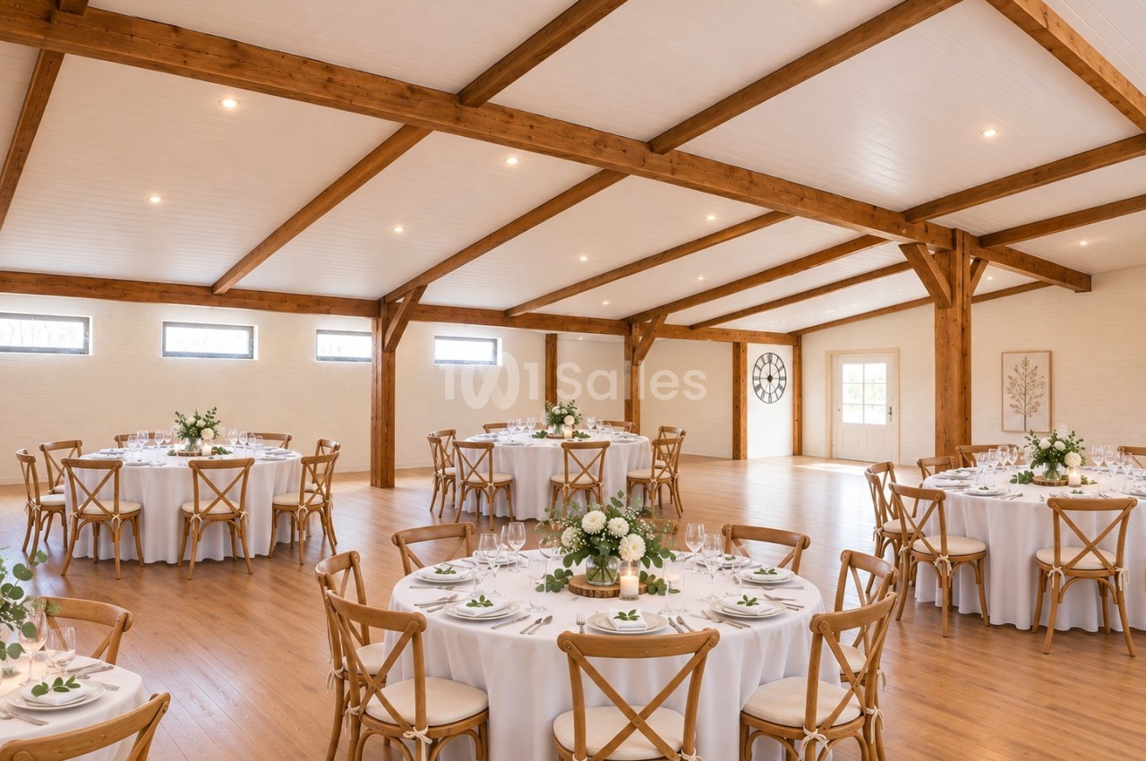 Salle intérieure avec poutres apparentes en bois, tables rondes dressées en blanc et chaises en bois clair.