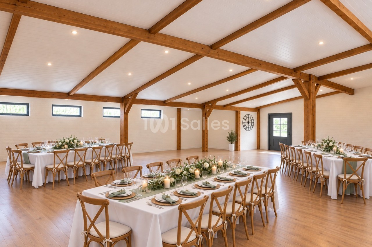 Salle élégante dressée pour mariage avec poutres bois apparentes, tables longues blanches et chaises en bois clair.
