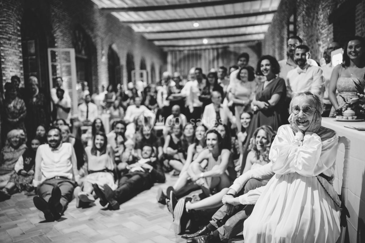 Un groupe de personnes souriantes posant dans une grande salle avec une femme âgée au premier plan.