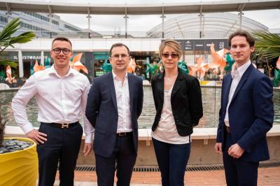 Un homme en costume bleu se tient debout sur une terrasse extérieure par temps nuageux.