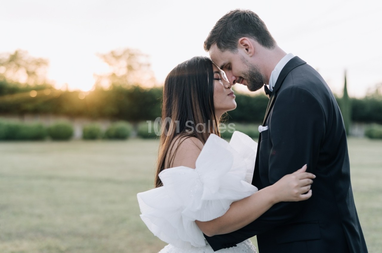 Un couple en tenue de mariage s'enlace tendrement dans un jardin au coucher du soleil.