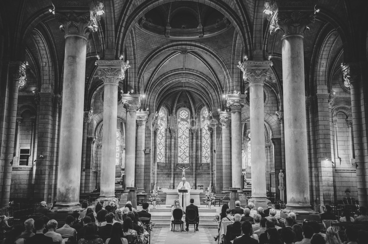 Intérieur d'une église avec des colonnes imposantes, des vitraux en arrière-plan et une cérémonie en cours.