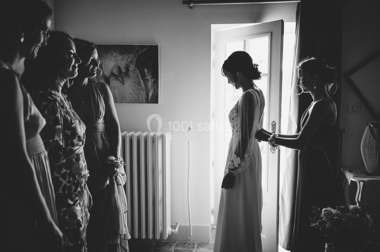 Une mariée se prépare entourée de proches dans une pièce éclairée par la lumière naturelle d'une porte ouverte.