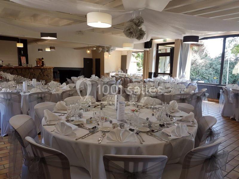 Salle de réception décorée avec des tables rondes dressées de nappes blanches et de vaisselle élégante.