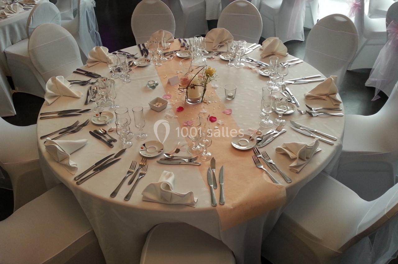 Table ronde élégamment dressée avec une nappe blanche, des couverts, des verres et une décoration centrale florale.