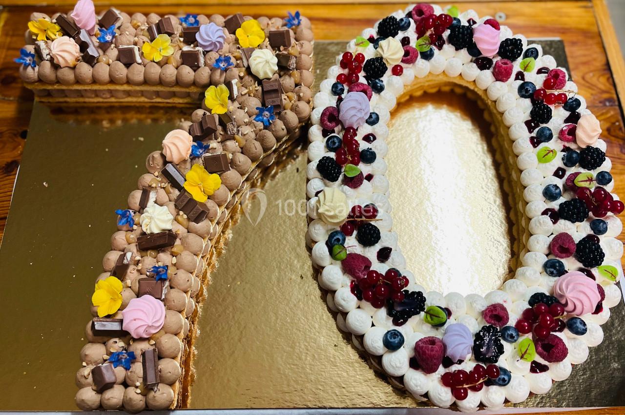 Gâteau en forme de ’70’ décoré de crème, fruits rouges, fleurs comestibles et morceaux de chocolat.