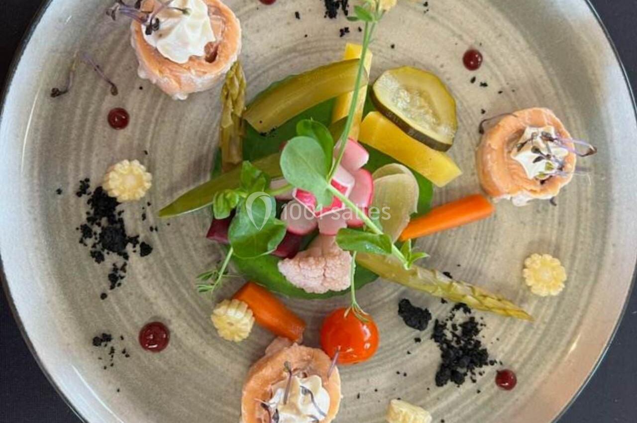 Assiette gastronomique composée de légumes colorés, saumon roulé et garnitures raffinées sur une table noire.