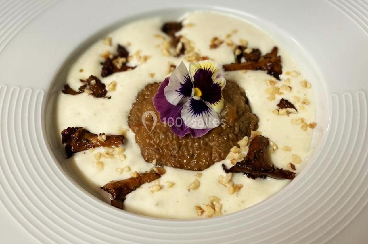 Plat gastronomique composé de risotto au centre, entouré de sauce crémeuse, champignons et décoré d'une fleur comestible.