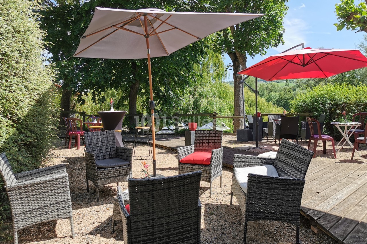 Mobilier de jardin en rotin avec parasols sur une terrasse extérieure entourée de verdure.
