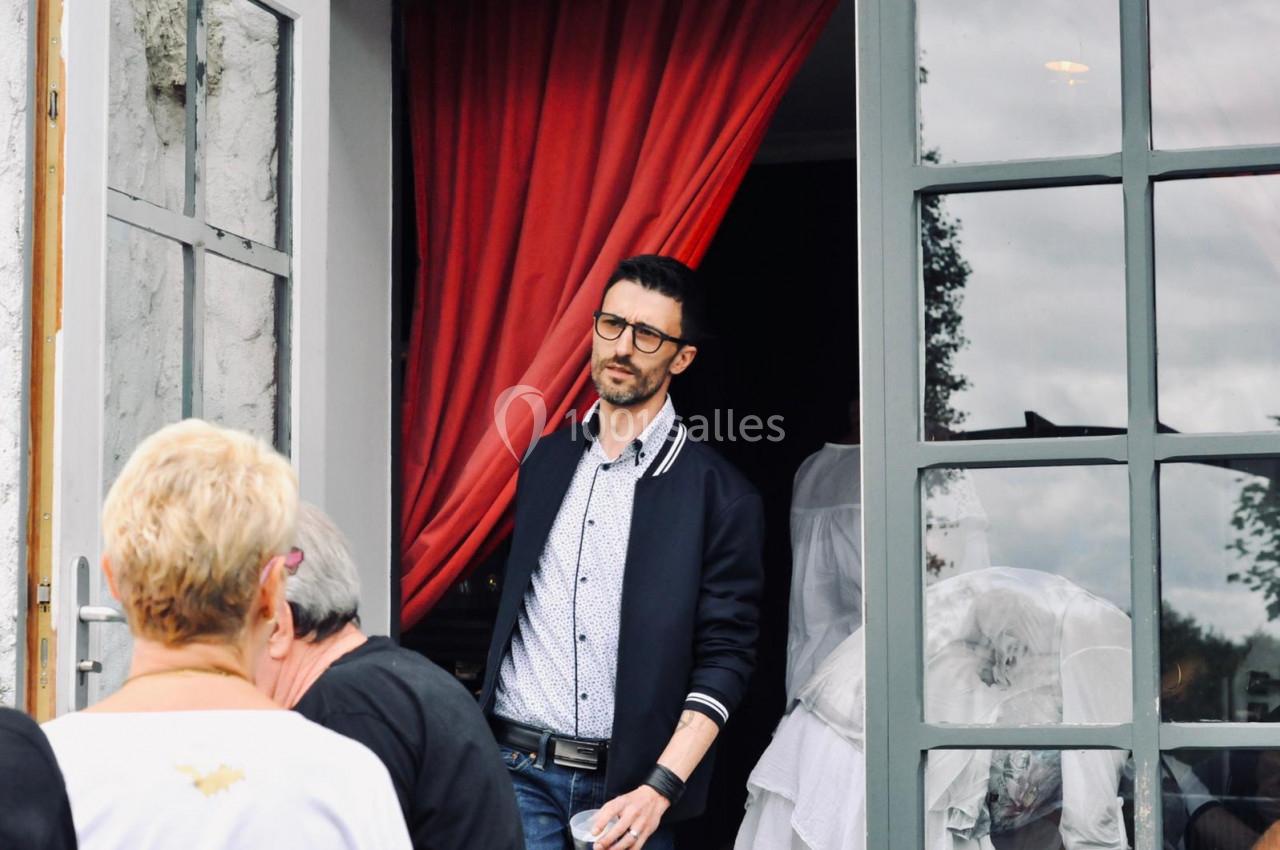 Un homme portant des lunettes sort d'un bâtiment avec des rideaux rouges, des personnes au premier plan.