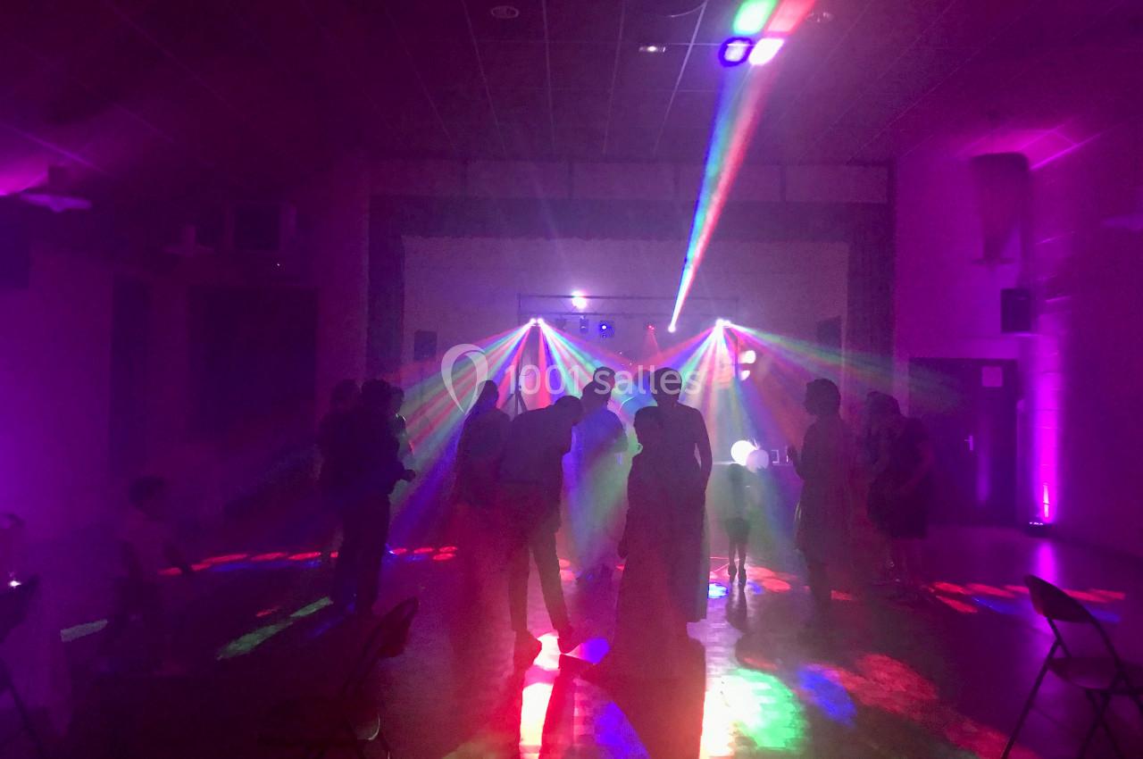 Personnes dansant dans une salle sombre éclairée par des faisceaux lumineux colorés provenant d'un jeu de lumières.