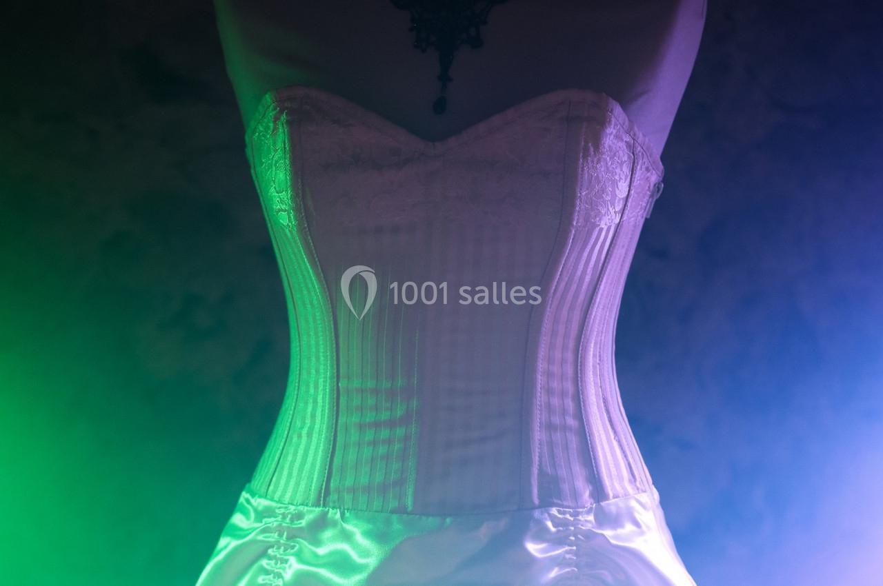 Corset blanc en dentelle et satin éclairé par des lumières vertes et violettes dans un environnement sombre.