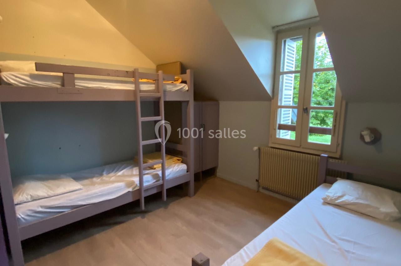 Chambre simple avec lits superposés, lit simple, fenêtre donnant sur un jardin, éclairage au plafond.