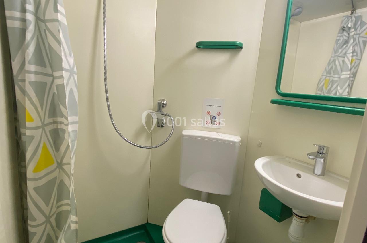 Salle de bain compacte avec douche, toilettes, lavabo, miroir et rideau de douche à motifs géométriques.