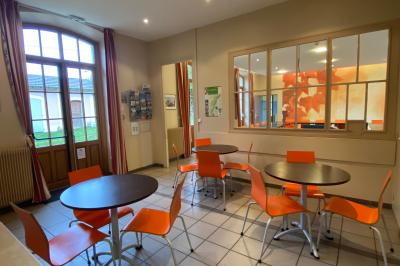 Miniature Location salle Sergenaux (Jura) - La Maison des Etangs #4 Salle de réunion lumineuse avec tables disposées en U et chaises orange, entourée de grandes fenêtres.