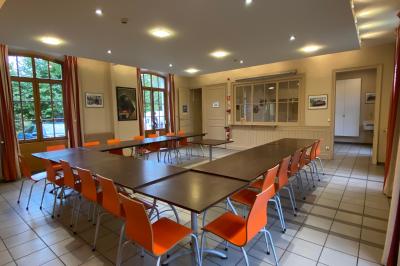 Miniature Location salle Sergenaux (Jura) - La Maison des Etangs #11 Salle de réunion lumineuse avec tables disposées en U et chaises orange, entourée de grandes fenêtres.