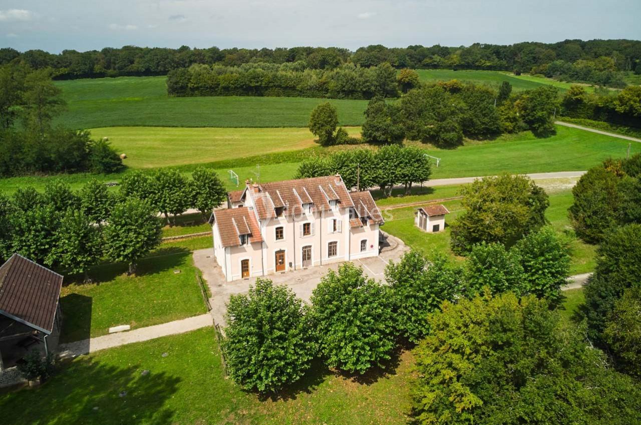 Vue aérienne d'une maison blanche à deux étages entourée d'arbres et de champs verdoyants.