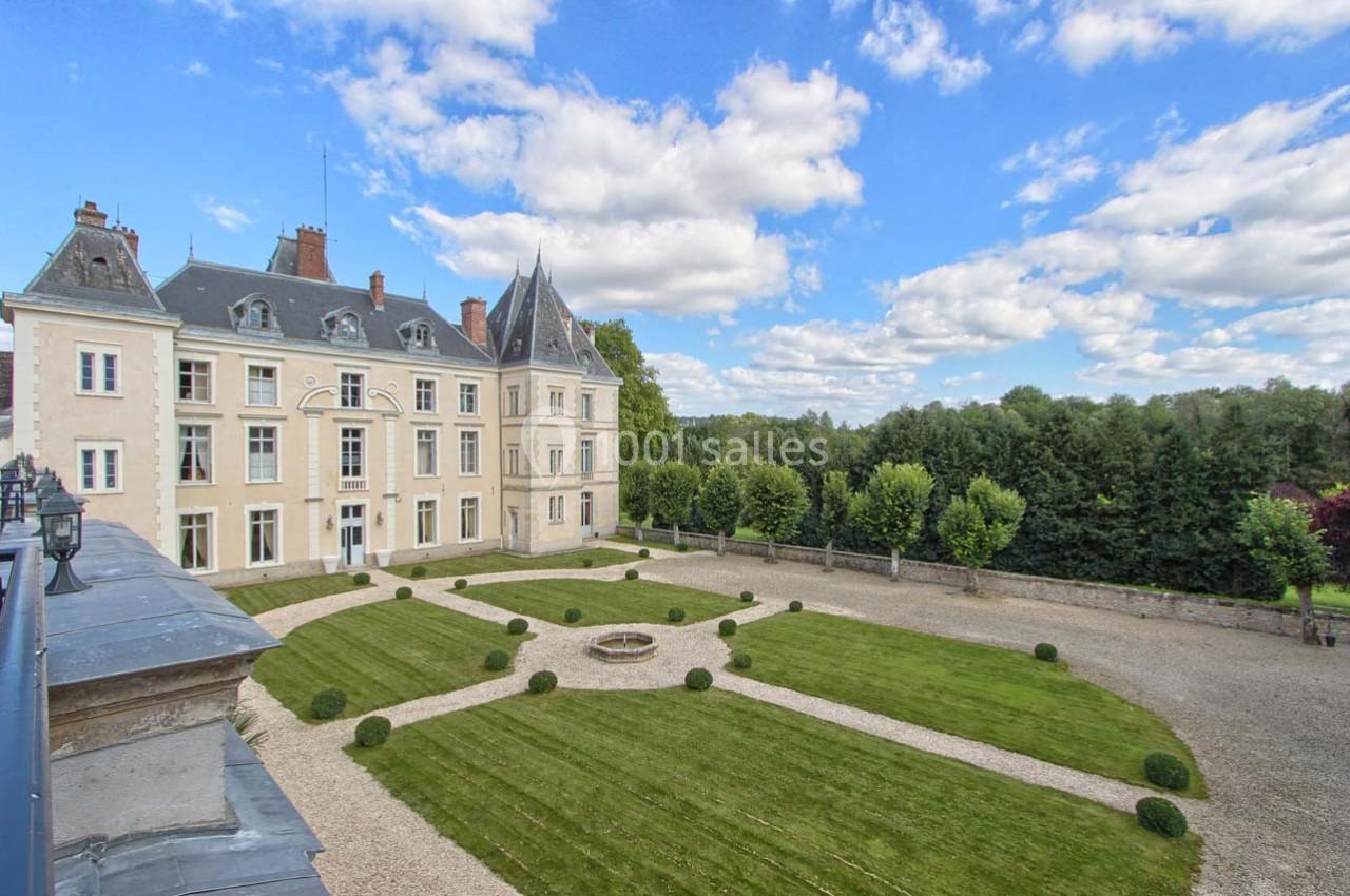 Façade d'un château historique entouré d'une cour avec pelouse, buis taillés et allées gravillonnées, sous un ciel…