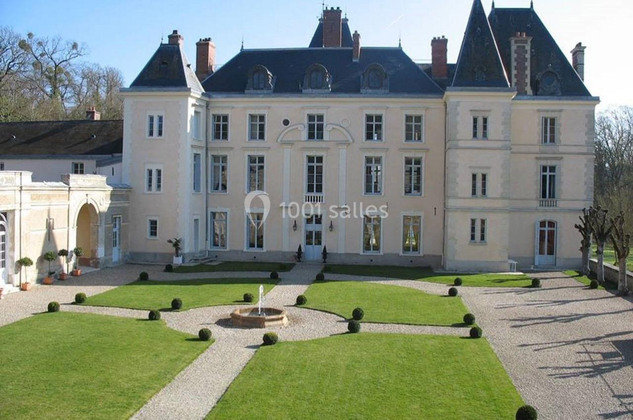 Façade d'un château avec toit en ardoise, entouré de jardins symétriques et allées gravillonnées.