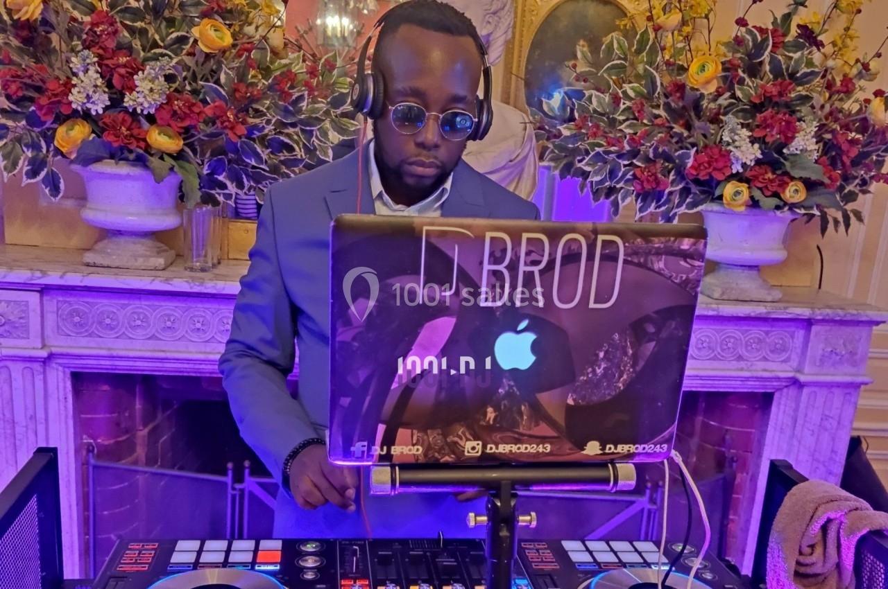 Un DJ en costume mixe de la musique sur une console devant une cheminée décorée de fleurs.