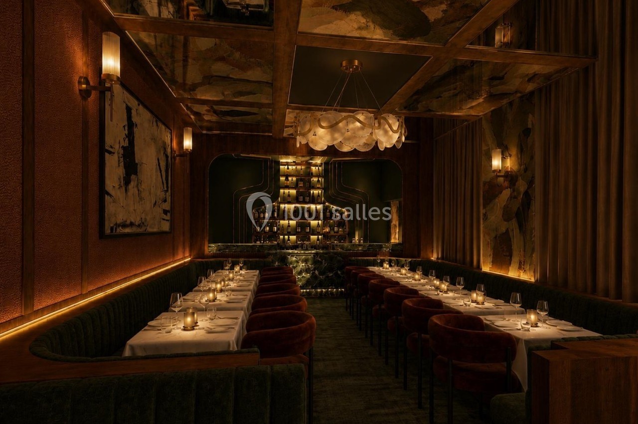 Salle de restaurant élégante avec longues tables dressées, éclairage tamisé et bar illuminé en arrière-plan.