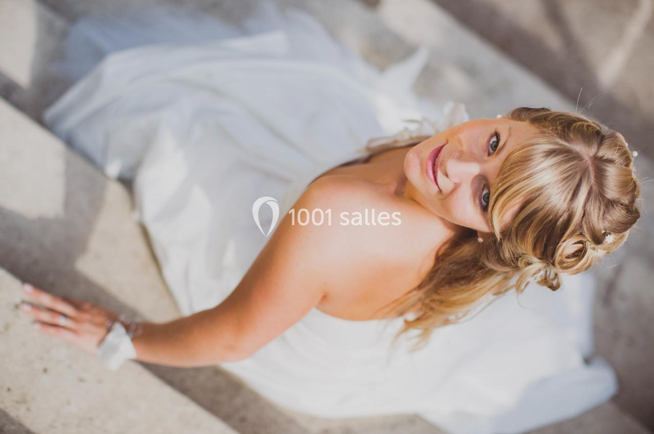 Femme en robe blanche assise sur des marches en pierre, regardant vers l'objectif avec une expression douce.