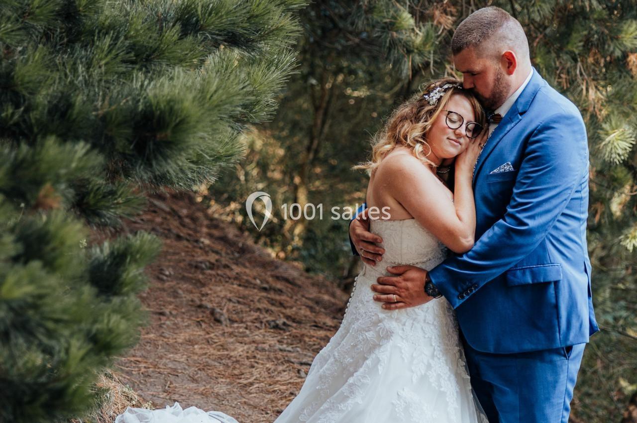 Un couple en tenue de mariage s'enlace tendrement dans une forêt, entouré de pins.