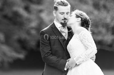 Miniature Au Bord des Yeux #2 Un couple s'embrasse en arrière-plan tandis qu'un bouquet de fleurs est mis au premier plan.
