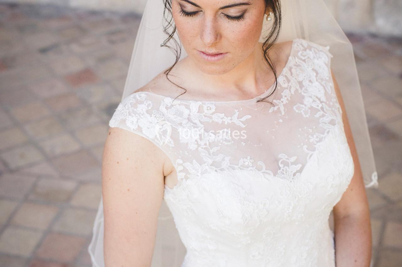 Femme en robe de mariée blanche avec un voile, regard baissé, sur un sol pavé.