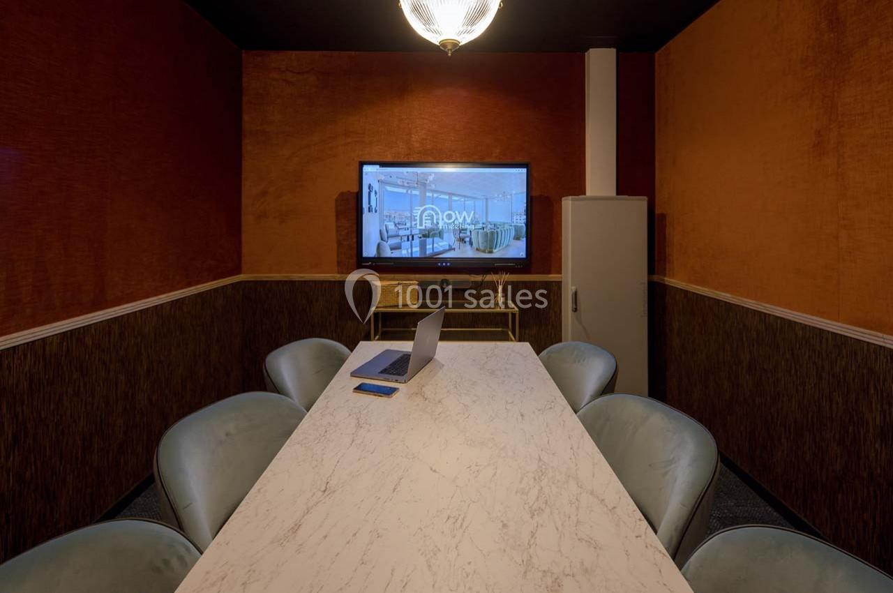 Salle de réunion avec table en marbre, chaises rembourrées, écran allumé et éclairage suspendu.