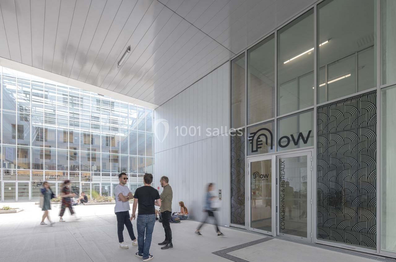 Entrée d'un espace de coworking moderne avec des personnes discutant dans une cour lumineuse.