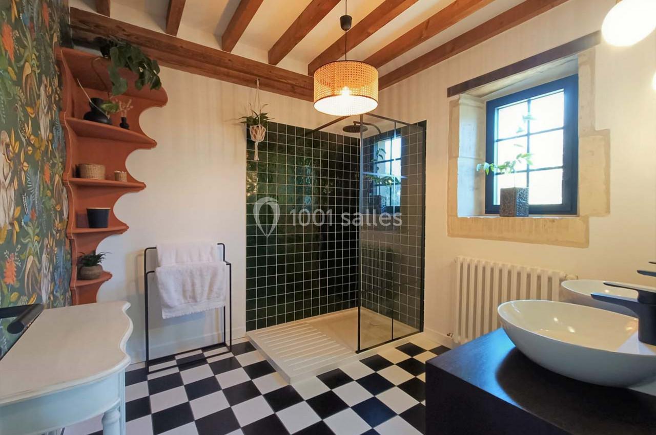 Salle de bain avec douche à l'italienne, carrelage noir et blanc, mur végétal, et poutres apparentes au plafond.