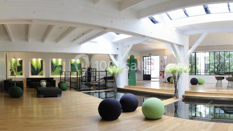 Espace lumineux avec parquet, mobilier moderne, plantes et grandes fenêtres laissant entrer la lumière naturelle.